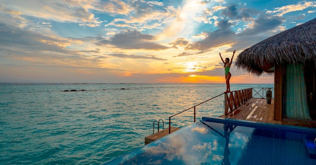 Woman enjoying a stunning sunset at a luxury Maldives resort's infinity pool.