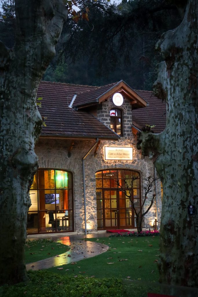 Cozy stone house glowing warmly amidst a twilight setting, framed by trees.